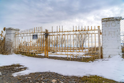 Fence on snow covered field against sky