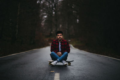 Full length of man sitting on road in forest