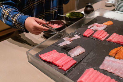 Midsection of man holding sushi in kitchen