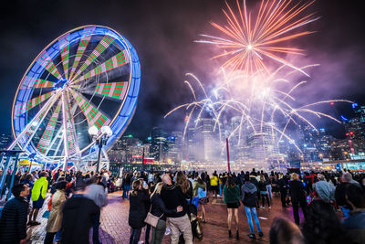 Firework display over illuminated city against sky at night