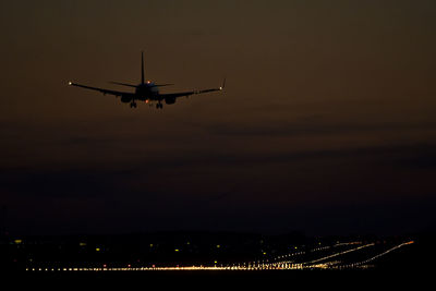 Silhouette airplane landing on illuminated runway at night