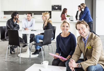 Portrait of happy business people with colleagues discussing in background at office restaurant