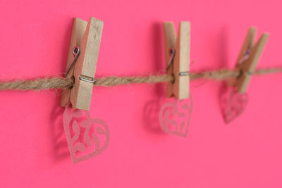 Close-up of heart shape hanging on rope against pink background