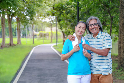 Portrait of smiling couple standing on footpath by field 