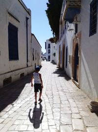 Full length rear view of woman walking on cobblestone