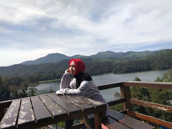 Full length of man sitting on bench against sky