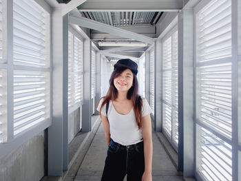 Portrait of young woman standing against window