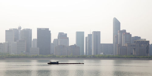 Boats in river by buildings in city against sky