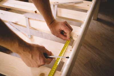 Cropped hands of man measuring wood at home