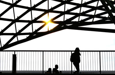 Silhouette people walking on railing against sky during sunset