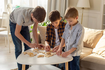 Three boys, in home enthusiastically play a board game made of wooden rectangular blocks