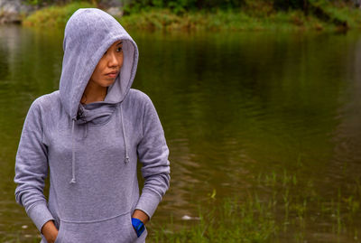 Beautiful woman with hands in pocket standing by lake