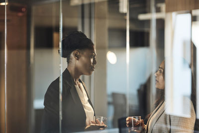 Side view of businesswomen discussing with each other in office seen through glass