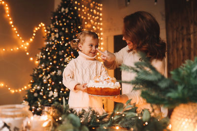 Mom and daughter, a child, prepare festive food in a decorated kitchen with a christmas tree at home