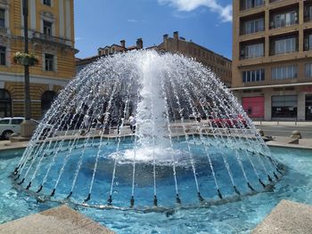 Water fountain in swimming pool against buildings in city