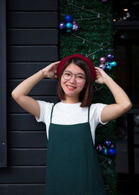 Portrait of smiling young woman standing against window during christmas