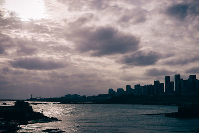 View of city at waterfront against cloudy sky