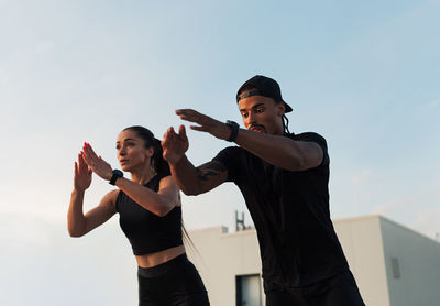 Portrait of young woman exercising with arms raised standing against wall