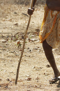 Low section of woman holding stick while walking on field