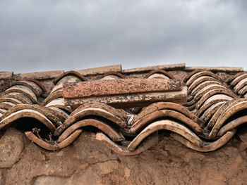 Low angle view of old roof tiles against sky