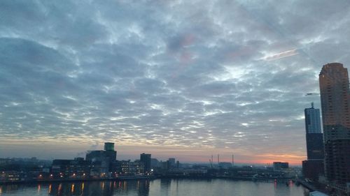 City by river against sky during sunset