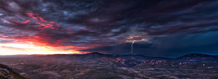 Scenic view of storm clouds over landscape during sunset