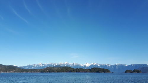 Scenic view of lake and mountains against clear blue sky