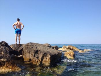Man standing on rock by sea against clear sky