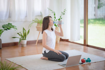 Young woman using phone while sitting on floor at home