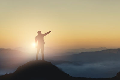 Silhouette man standing on mountain against sky during sunset