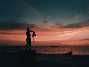 Silhouette people on beach against sky during sunset