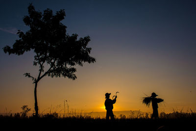 Silhouette farmers harvesting on field against sky during sunset