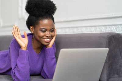 Smiling young woman using laptop at while lying on sofa at home