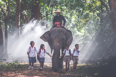 School children walking by elephant in forest