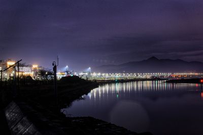 Illuminated bridge by sea against sky at night