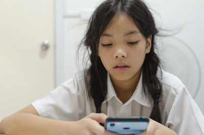 Girl using mobile phone against wall