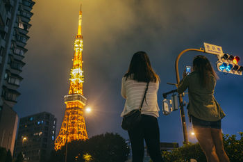 Rear view of woman photographing illuminated tokyo tower against sky at night