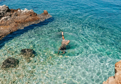 High angle view of young woman in black bikini swimming in transparent sea water.