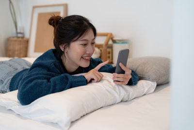 Woman using smart phone lying on bed