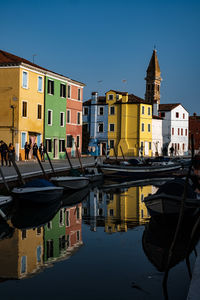 Boats moored on canal by buildings against sky