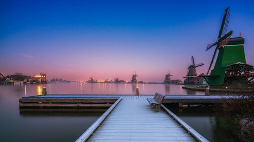 View of pier by windmills against sky during sunset