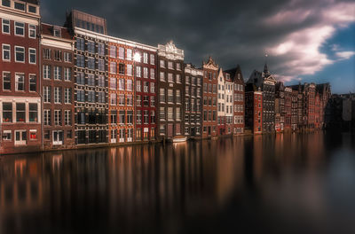 Buildings by river against sky in city