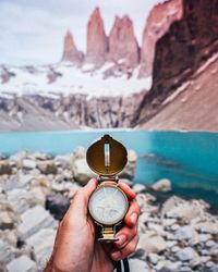 Close-up of man holding navigational compass against lake and mountain