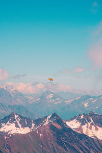 Helicopter flying over rocky mountains against blue sky