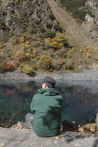 Rear view of man sitting by lake against mountain