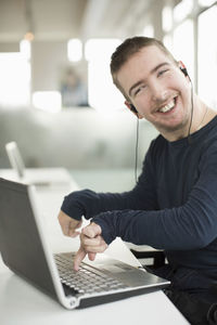 Portrait of happy businessman with cerebral palsy using laptop while listening music