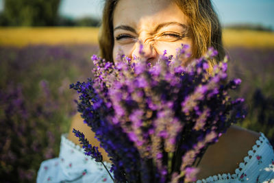 Close-up happy woman face with purple lavender flowers in summer field.