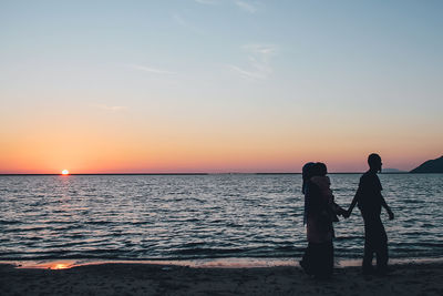 Woman standing on beach against sky during sunset