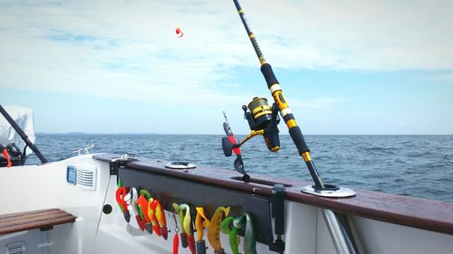 Fishing rod on boat by sea against cloudy sky