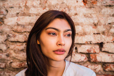 Close-up portrait of a young woman against brick wall